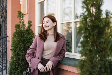 young pleased woman with red hair standing near building.