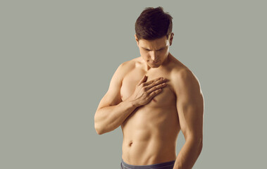 Fototapeta premium Naked sexy young man model in underwear isolated on grey studio background suffer from heart attack or disease. Toned muscular guy have pain in chest struggle with cardiovascular illness.