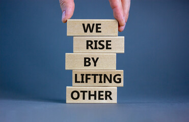We rise by lifting other symbol. Concept words We rise by lifting other on wooden blocks. Businessman hand. Beautiful grey table grey background. Business we rise by lifting other concept. Copy space.