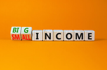 Big or small income symbol. Turned wooden cubes and changed concept words Small income to Big income. Beautiful orange table orange background, copy space. Business big or small income concept.
