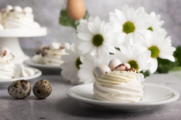 Meringue desserts with quail egg toppings alongside white daisies on a textured gray background.