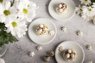 Obraz na płótnie Canvas A showcase of meringue treats and quail eggs set against white daisies and a neutral gray backdrop.