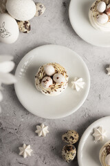 Meringue. Meringue treats with quail eggs and chocolate details on white plates, gray surface backdrop. Easter day.