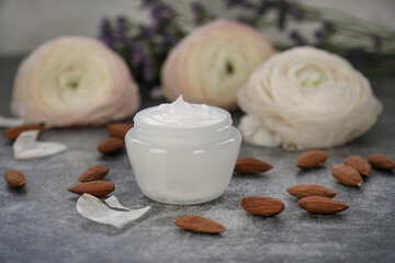 Fototapeta na wymiar Face or body cream with almonds on grey background with real flowers. 
