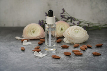 Obraz na płótnie Canvas Almond water in glass dropper bottle for skin care on grey background with almonds nuts and flowers. 