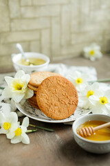 Honey cookies with natural patterns on a plate on a dinner table with flowers and tea. Food photography in light colors with cookies and spring daffodils.