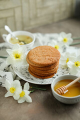 Naklejka na ściany i meble Honey cookies with natural patterns on a plate on a dinner table with flowers and tea. Food photography in light colors with cookies and spring daffodils.