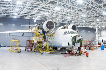 White transport aircraft in the hangar. Airplane under maintenance. Checking mechanical systems for...