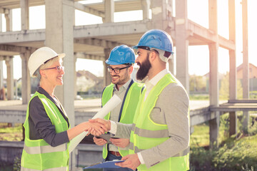 Happy mixed group of young architects talking and shaking hands during meeting on a construction site