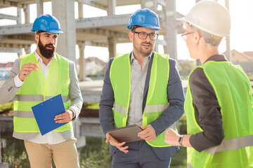 Mixed team of young architects or engineers meeting on a construction site, discussing building progress and plans