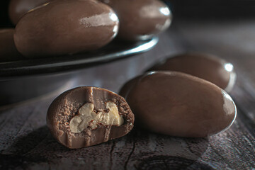 Milk chocolate covered nuts on a black plate and over a rustic wooden table macro dark food photography horizontal side view shot