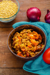 A plate of bulgur with vegetables and mushrooms on a blue napkin next to tomatoes onions and a cup of bulgur on the table.