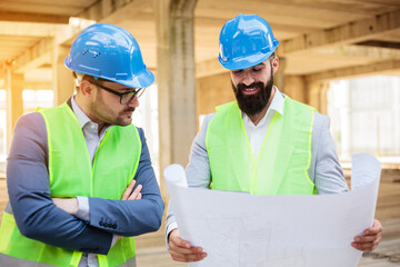 Two young male engineers or business partners at a construction site, discussing project details. Architecture and teamwork concept.
