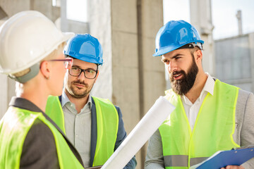 Mixed team of young Caucasian architects and engineers meeting on a construction site, looking at progress reports and talking