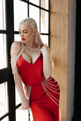 Young slim sexy and attractive blonde woman in a red dress at the window