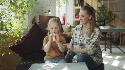 A little girl plays the flute with a tutor. The woman prompts her and instructs