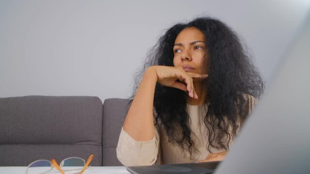 Young adult black woman thinking about problem solution. Portrait of a pensive POC female filmed in thought in front of a computer