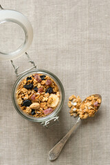 A glass jar with homemade granola on a fabric linen background. Granola with nuts and dried fruits...