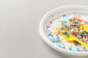 Microplastic in white plastic dish with knife and fork. Light grey background. Microplastic problem concept. Place for text