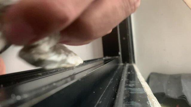 Hand with tissue wiping dry filthy dirt on sliding door bottom track black rail of residential apartment home. Daily chores concept - close up 