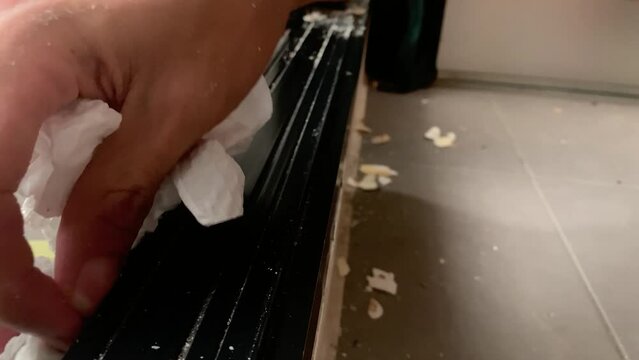 Hand with tissue wiping dry filthy dirt on sliding door bottom track black rail of residential apartment home. Daily chores concept - close up 