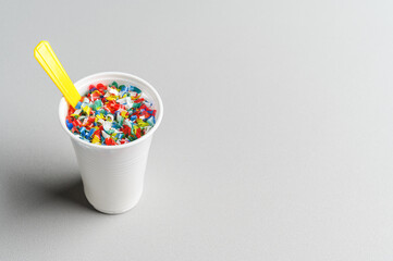 Microplastic in white plastic cup with spoon. Light grey background. Microplastic problem concept. Place for text