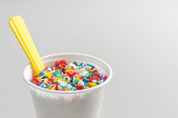 Microplastic in white plastic cup with spoon. Light grey background. Microplastic problem concept. Place for text