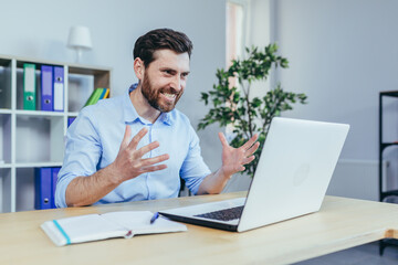 Fototapeta premium An angry businessman looks at the laptop screen and shouts, working in a bright office