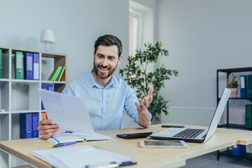 Happy businessman working with papers, working on laptop, man at work in a bright office