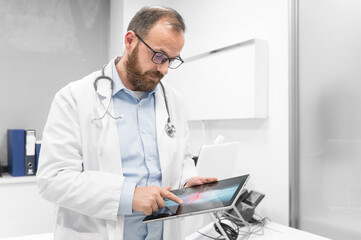 Fototapeta premium Doctor examine an x-ray image of a patient in digital tablet at doctor office. High quality photography.