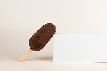 Chocolate ice cream bar with sticks. Popsicle and lolly sweet dessert on white platform with copy space. Geometric shapes podium with ice cream. Summer creative food concept.