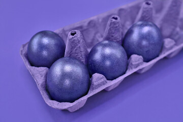 Violet four colored eggs in purple egg paper box on violet background. Painted Easter eggs in shiny very peri trendy color of 2022 year. Happy Easter concept. Shopping, supermarket, organic farm food.