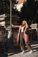 full length of sunshine on face of cheerful young woman in coat holding handbag.