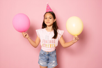 Smiling adorable little child girl posing with pastel pink air balloons isolated over pink...