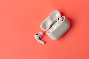 Top view white wireless headphones for smartphone vith charging case on coral background. The concept of modern technology, gadgets.