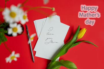 Obraz premium Mother's Day message with flowers and candies. Congratulations on mother's day with a card and spring flowers yellow tulip on a red flat lay background.