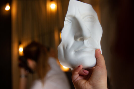 clay white mask in the hands of a girl. white mask in the form of a human face.