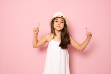 Obraz na płótnie Canvas Cheerful little kid girl years old in white dress isolated on pink background children studio portrait. Childhood lifestyle concept. Mock up copy space. Pointing index fingers up