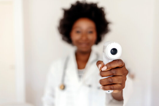 Professional female doctor wearing a white coat, showing digital thermometer isolated on white background. Doctor ready to use infrared forehead thermometer (thermometer gun) to check body temperature