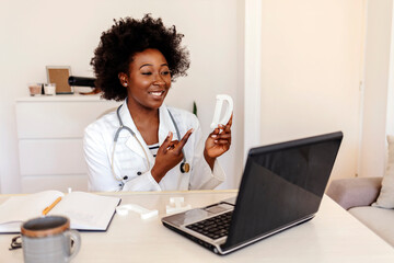 Cropped shot of a young African American speech therapist holding letters in hands while conducts an online lesson with a laptop webcam.