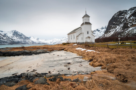 The small wooden white church in Gimsøy on the beach on the Lofoten islands in Norway in winter with beautiful old cemetary and mountains Vagan Nordland Norway