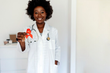 African woman wearing doctor uniform holding support red ribbon smiling at camera. Medical health...
