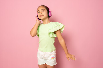 Beautiful cute happy little girl with headphones standing isolated over pink background.