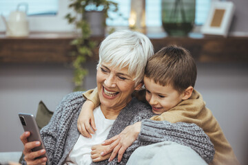 Grandma and grandson spend time together watching a funny video or cartoon on the phone, laughing...