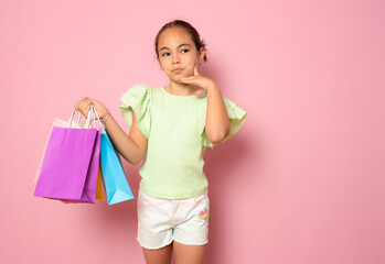 Sale. Cute little girl with many shopping bags on pink background. Portrait of a kid on shopping....