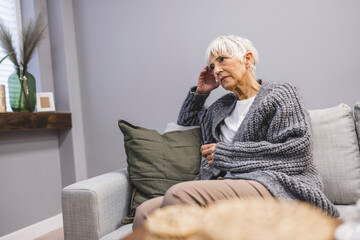 Attractive middle aged woman sitting on the couch (negative emotions). Upset mid-age woman sitting on sofa indoors. She is concerned about something or having headache.