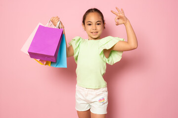 Sale. Cute little girl with many shopping bags on pink background. Portrait of a kid on shopping....