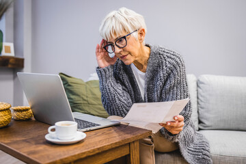A senior mature business woman who keeps a paper account using a laptop, an old woman manages the finances of the account, calculates the tax on the cash budget, plans to pay off the bank loan debt