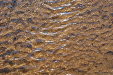 The bottom of the river with fine sand. Current, waves and wind. Water background. Sun glare.