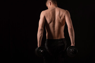 Naklejka na ściany i meble young handsome muscular man doing exercises with dumbbells on a black background